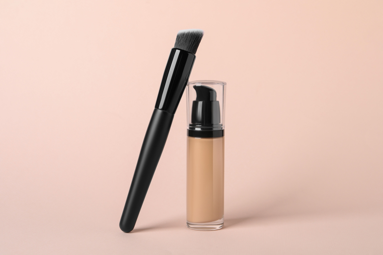 Bottle of skin foundation and brush on beige background. Makeup product