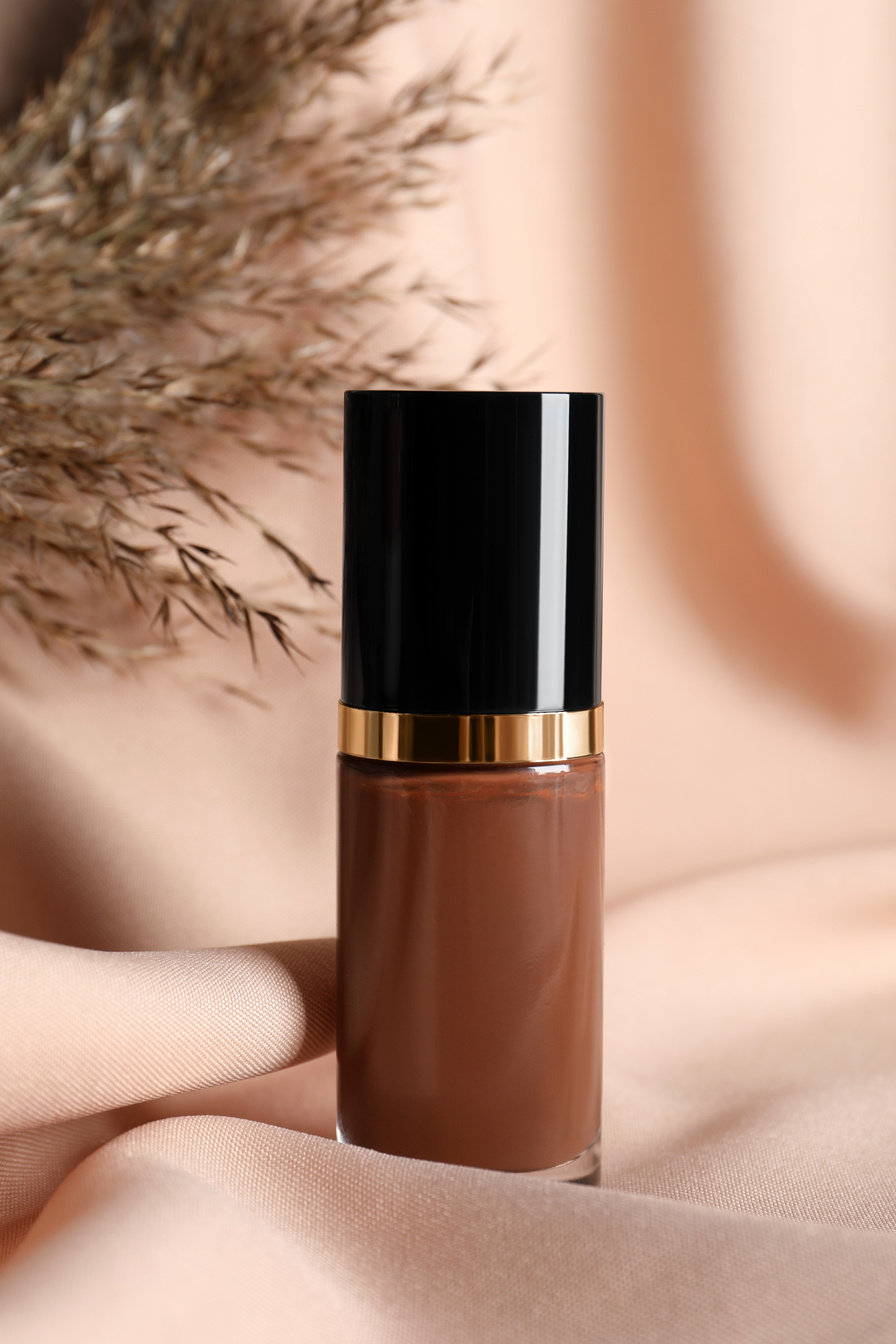 Bottle of skin foundation and dried reed on beige cloth. Makeup product